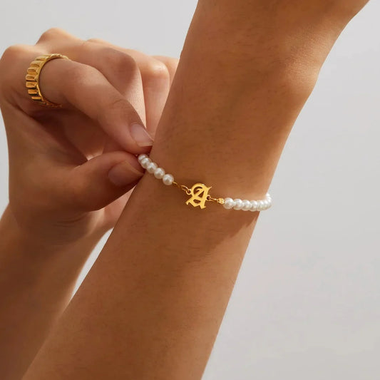 Close-up on model's wrist highlighting the A initial charm on the Eraya Jewel Pearl Bracelet gold polish