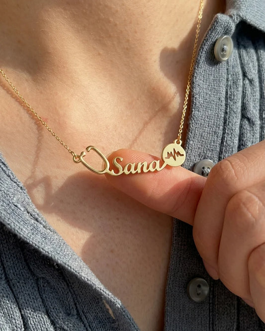 Custom “Sana” doctor name necklace with stethoscope and heartbeat detail in a minimal gold finish, styled on skin with natural lighting.