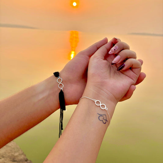 Couple wearing infinity bracelets at sunset, sharing a romantic moment
