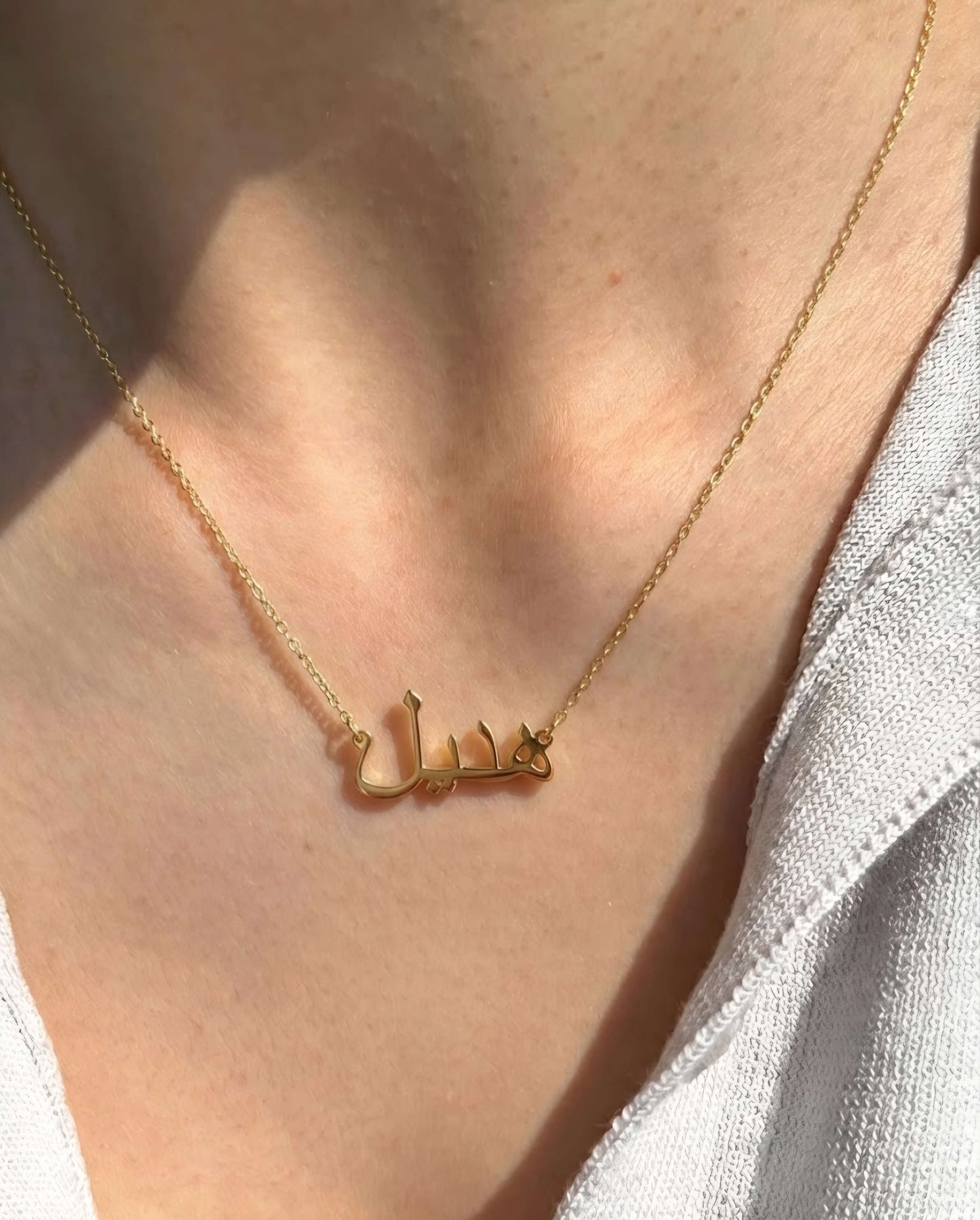 Sleek Arabic name necklace in polished gold finish, minimal custom Arabic script pendant on fine chain, luxury personalized jewelry aesthetic