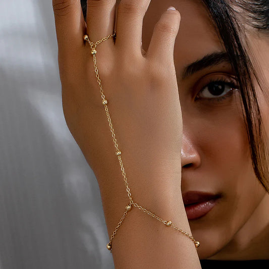 Model's hand gracefully adorned with the Golden Sheen Hand Harness, showcasing its elegant gold-plated chain draping from wrist to ring.