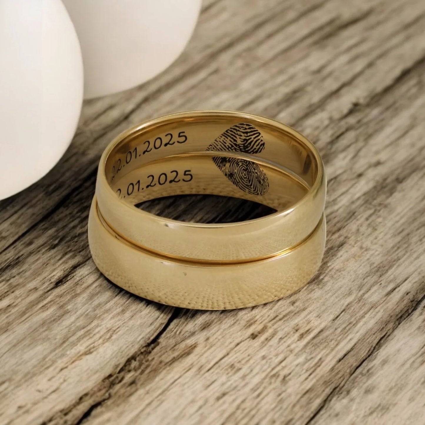 A close-up view of two gold rings from the Eraya Jewel "Custom Name and Fingerprint Couple Rings" set, showcasing the engraved fingerprints and the date "22.01.2025" on one ring and "2.01.2025" on the other.
