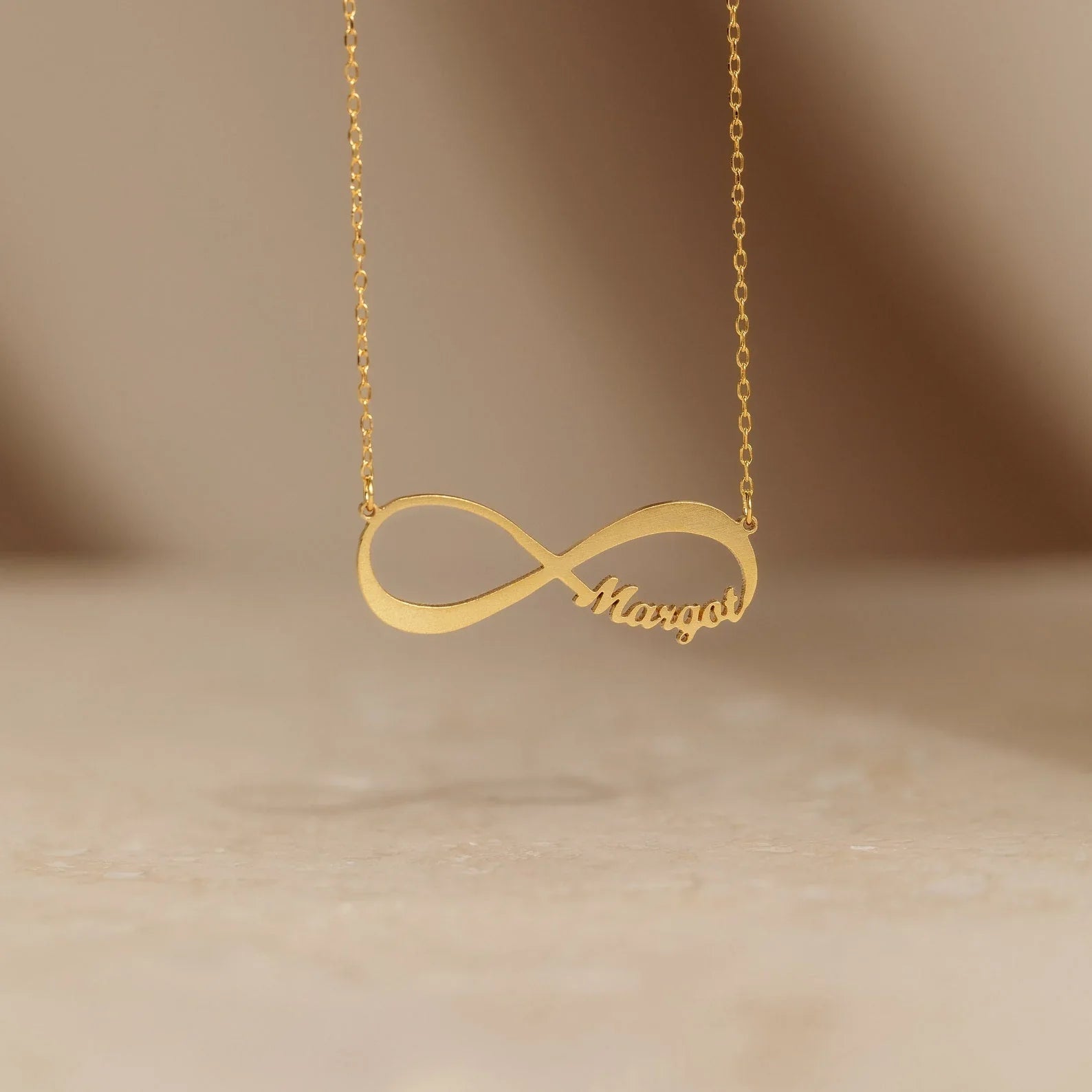 Detailed view of the gold Personalized Infinity Necklace, featuring elegant engraved words on a modern infinity pendant