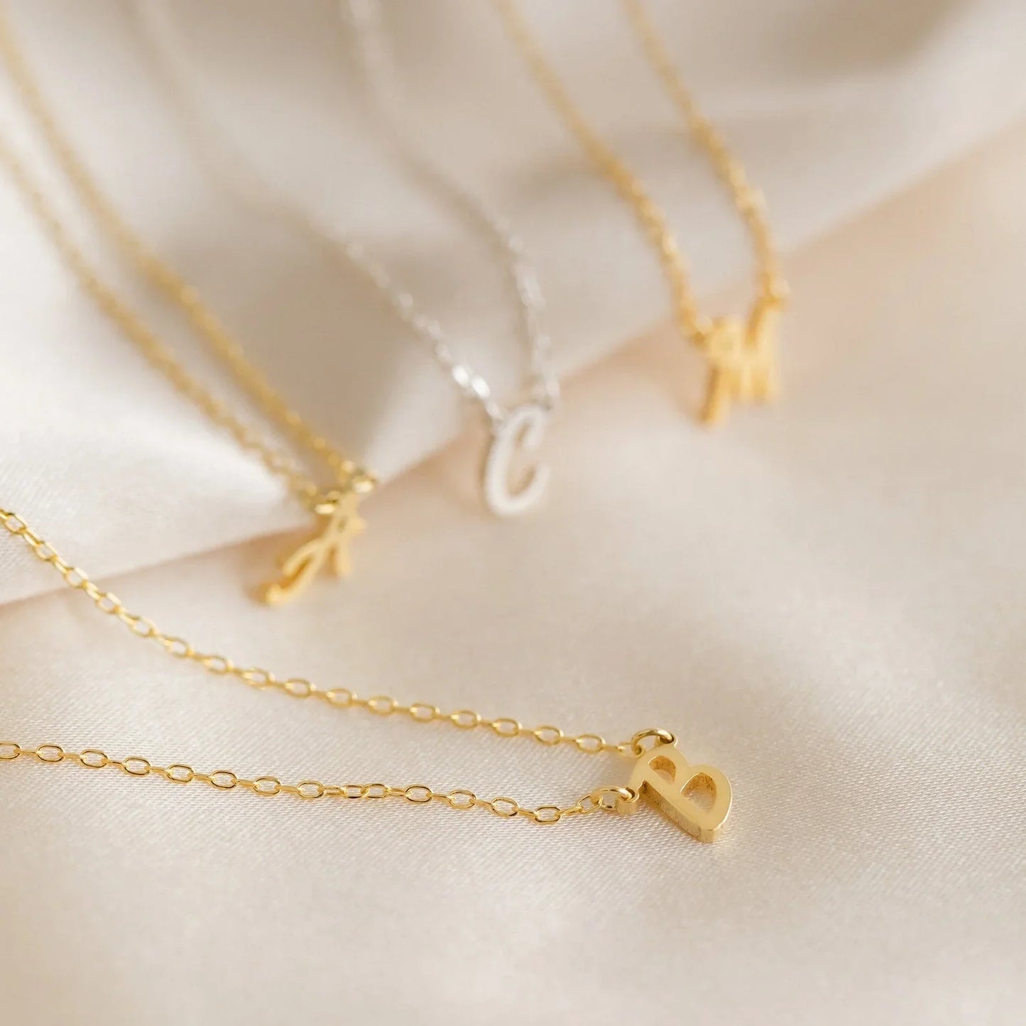 A collection of Eraya Jewel Initial Letter Pendants featuring the letters 'A,' 'B,' 'C,' and 'M,' demonstrating the variety of options available for personalization.