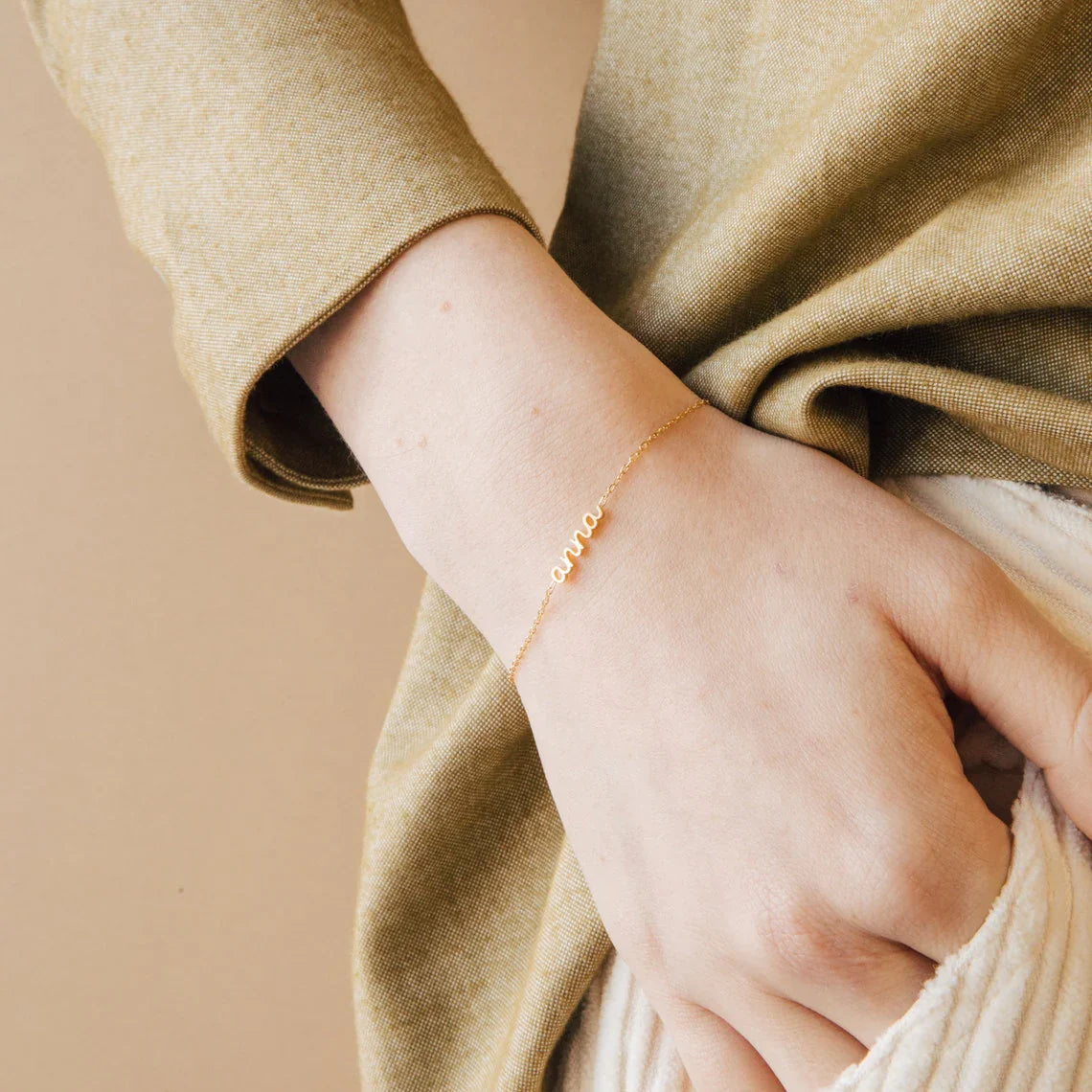 Model's wrist adorned with a chic stack of Eraya Jewel Dainty Layering Name Bracelets, possibly in mixed Gold and Silver finishes.