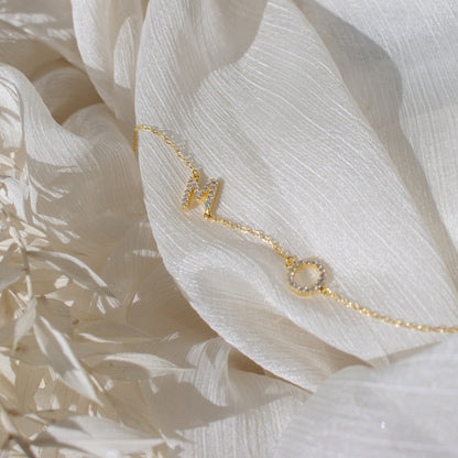 Close-up of CZ pavé couple initial necklace with M and O initials on white fabric