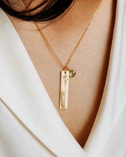 Close-up detailing the custom engraving on an Eraya Jewel gold personalized birth flower, name, and birthstone pendant, highlighting the floral artwork and green peridot charm.