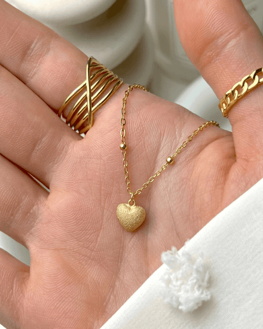 close up of minimal gold heart pendant with textured finish