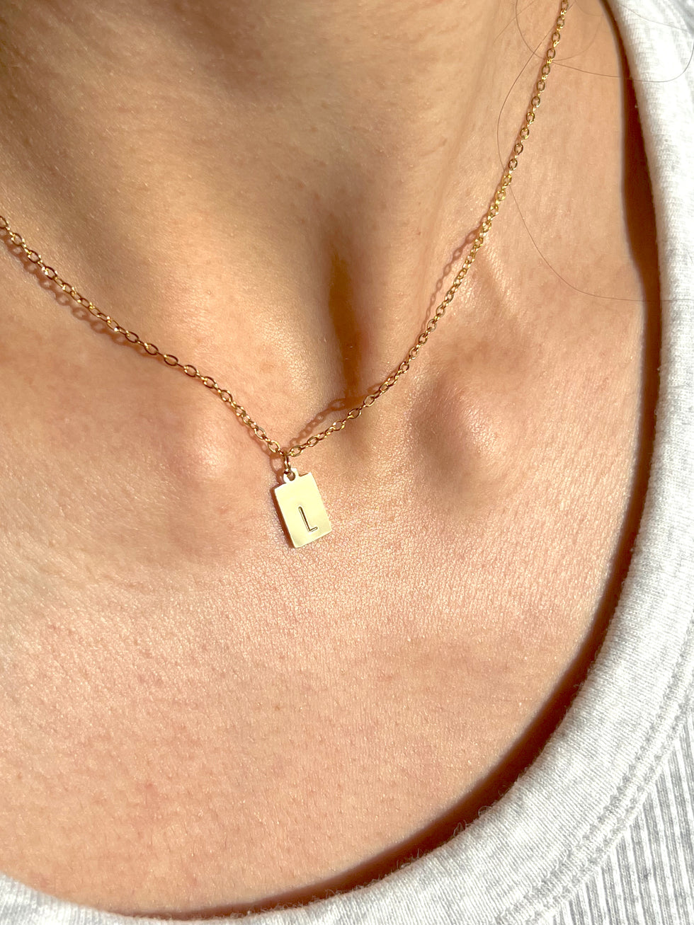 Woman wearing tiny rectangle initial pendant – minimalist dainty letter necklace close-up