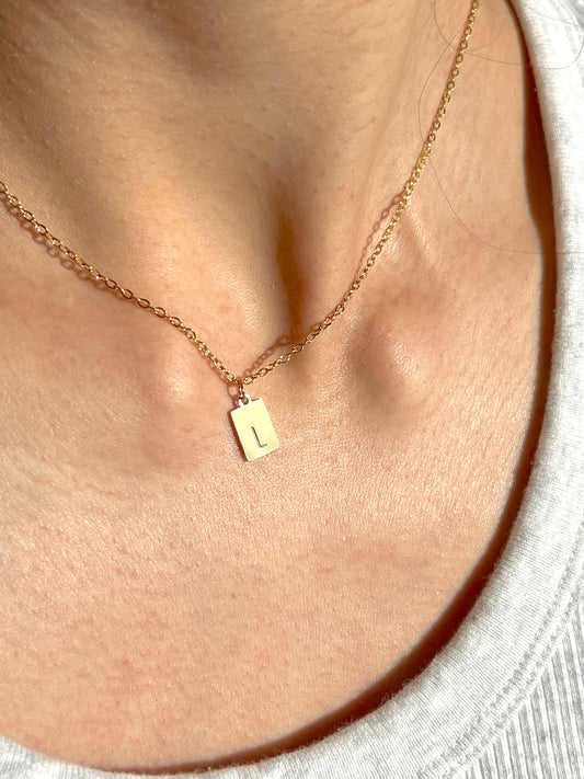 Woman wearing tiny rectangle initial pendant – minimalist dainty letter necklace close-up