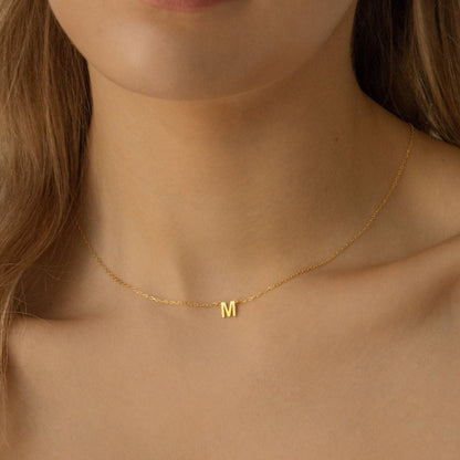 Gold necklace with a 'M' pendant on a person's neck