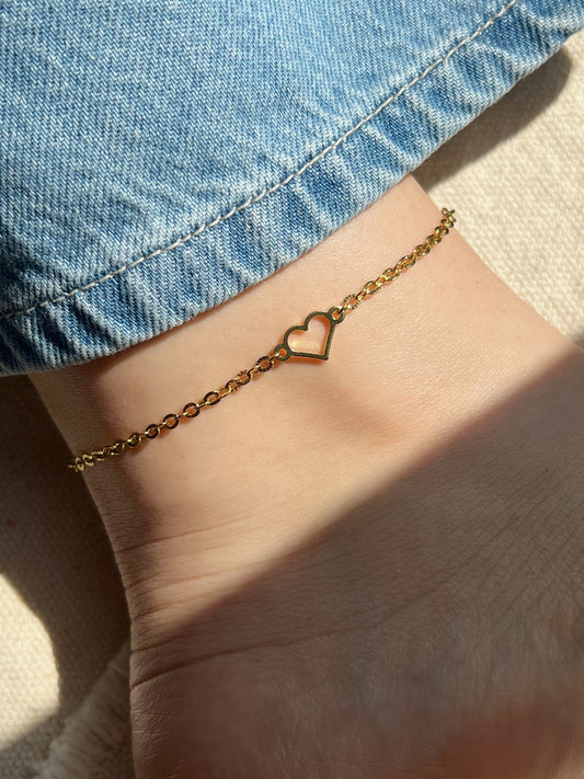 Close-up of a gold anklet with a heart charm shining on the ankle in natural sunlight.