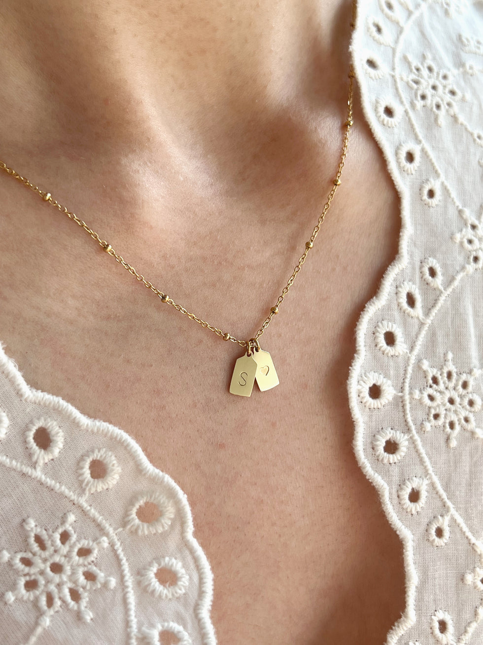 Model wearing gold heart pendant with initials, close-up on neck