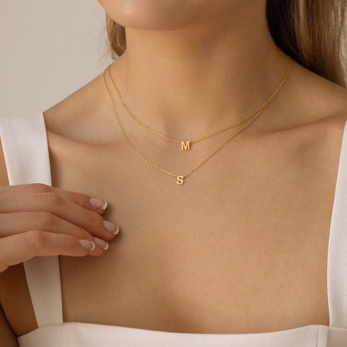 Gold necklace with letter pendants on a person wearing a white top.