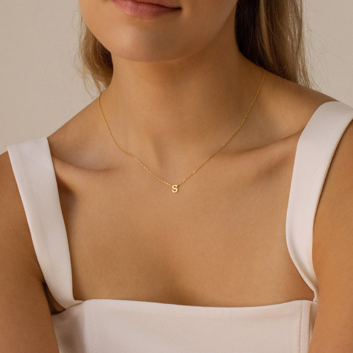 Woman wearing a gold necklace with a 'S' pendant against a neutral background